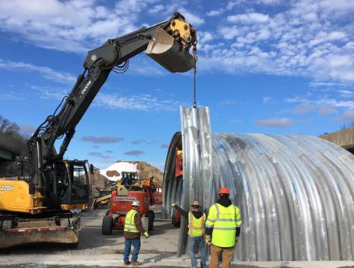 The crane is lifting the corrugated metal pipe on the construction site.