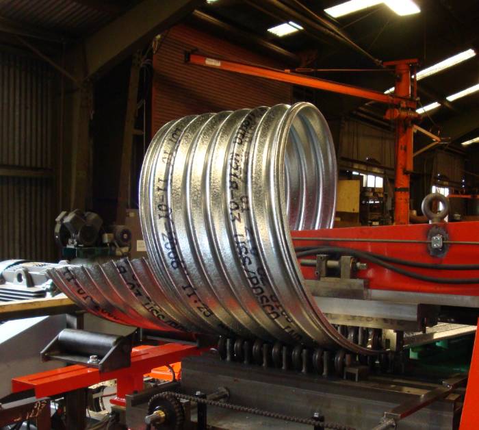 The machine is producing corrugated metal pipes.